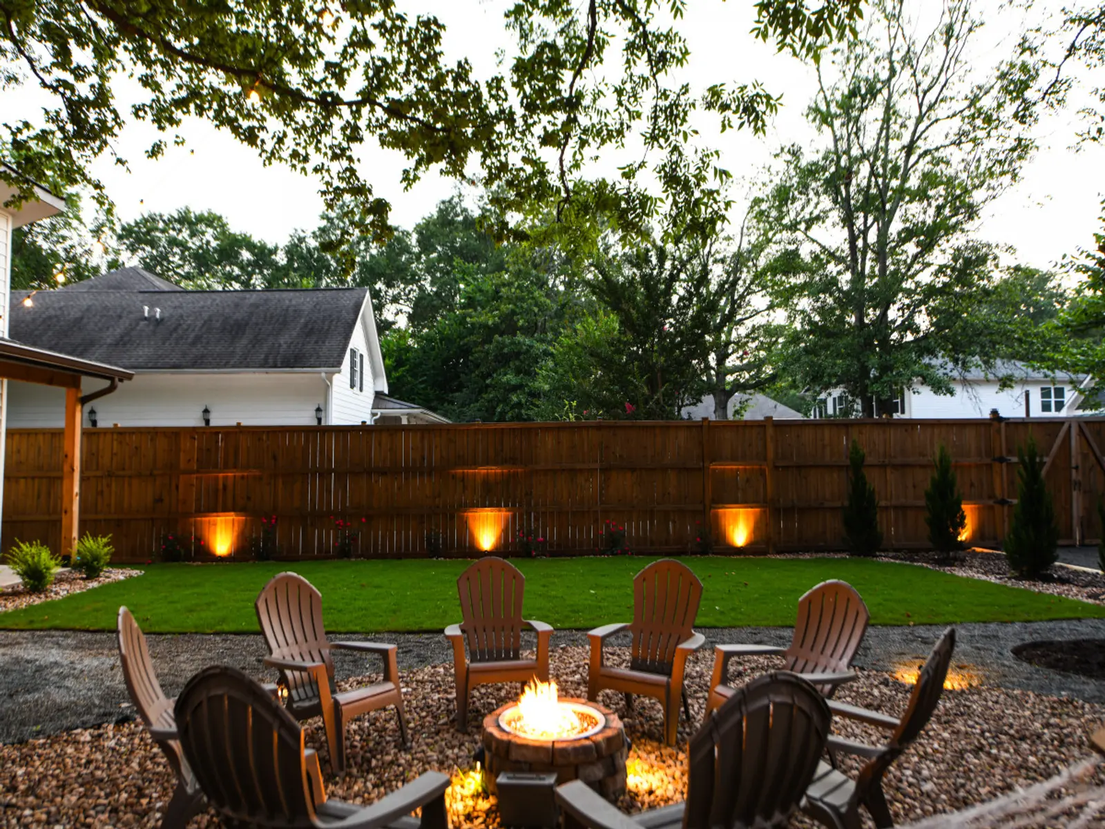 Fenced backyard with Adirondack chairs around the gas fire pit