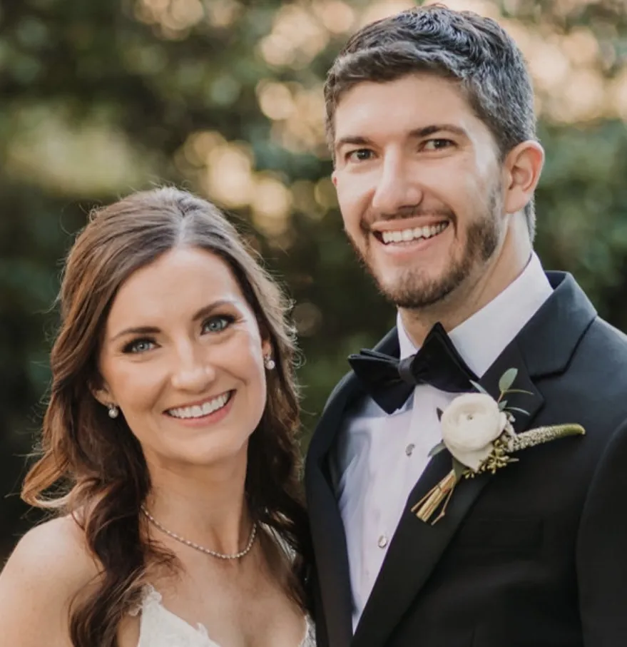 Daniel and Catherine smiling together on their wedding day, she in a white dress and he in a tuxedo with a white boutonniere